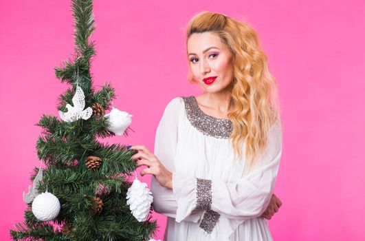 Christmas and holiday concept - Portrait of smiling beautiful blonde woman with Christmas tree on pink background.