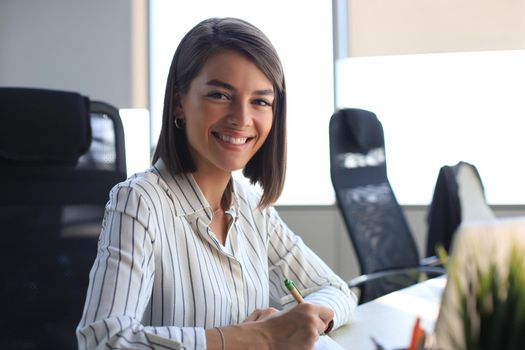 Beautiful business woman is writing something down while sitting in the office desk.