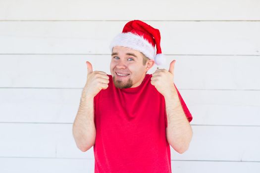 Christmas and people concept - cheerful young man in christmas hat showing thumbs up on white background.