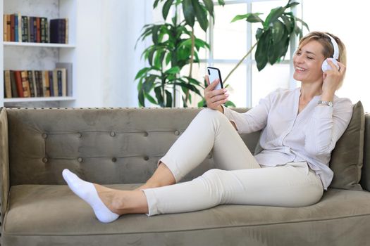 Beautiful middle aged woman relaxing in sofa using smartphone and earphones