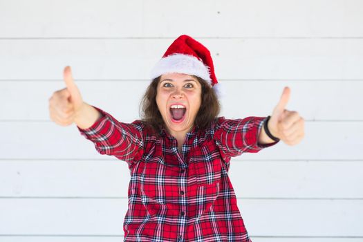 Christmas and people concept - woman in christmas hat showing thumbs up.