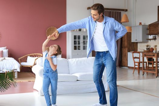Handsome young man dancing at home with his little cute daugther