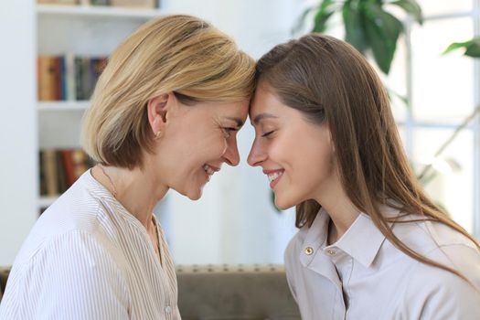 Happy middle aged mother and daughter talking on sofa in living room