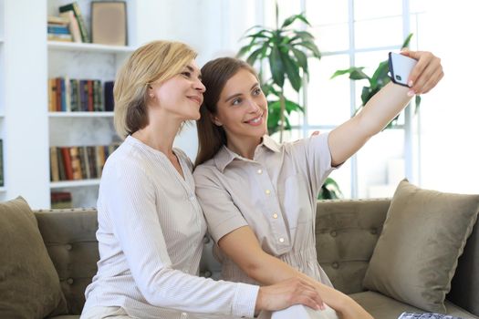 Happy middle aged mother and daughter taking selfie at home