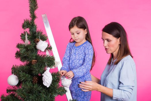 Christmas of young mom and her daughter with Christmas tree on pink background.