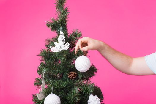 December and holidays concept - Man's hand decorating Christmas Tree on pink background.