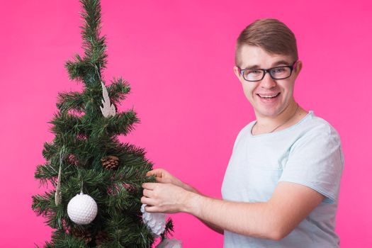 people, holidays and christmas concept - young smiling man near christmas tree on pink background.