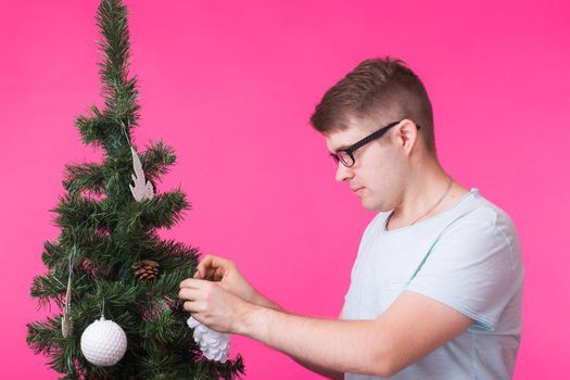 People, holidays and christmas concept - young man decorating christmas tree on pink background.