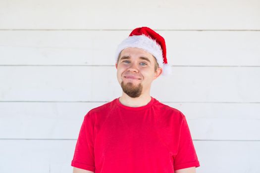 Christmas, holidays, people concept - young man in santa hat and shirt smiling over the white background.