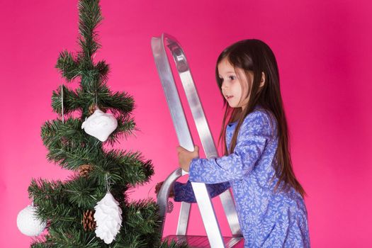 Christmas and holiday concept - A little girl is decorating Christmas tree