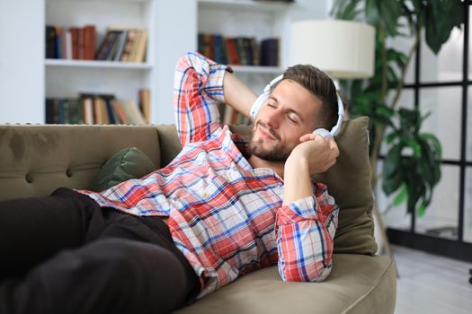 Young hipster man lies on the couch and listens to music in wireless headphones