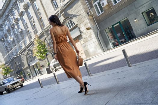 Full length of a young fashionable woman wearing long romantic dress and high heel shoes walking on the city streets, rear view. Fashion, people lifestyle concept