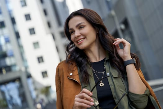 Fashionable girl spending time outdoors. Young beautiful and happy stylish woman with eyeglasses in hand standing on the city street and smiling. Urban lifestyle concept, business people