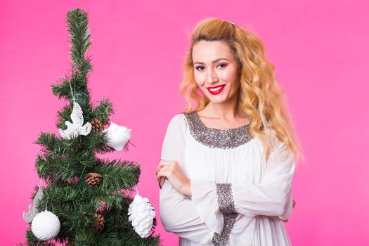Holidays concept - Blonde woman near christmas tree on pink background.