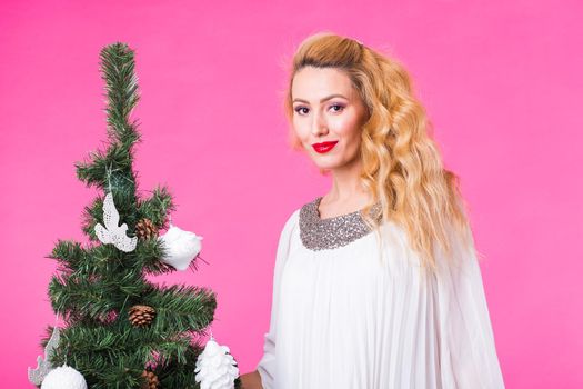 Holidays concept - Blonde woman near christmas tree on pink background.