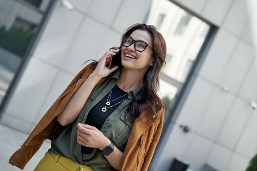 Enjoying nice talk. Young beautiful and stylish woman talking on smartphone with friend and smiling while walking on the city street. Urban lifestyle concept, people