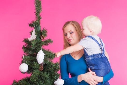 Christmas, holidays and people concept - woman and her kid near christmas tree over pink background.