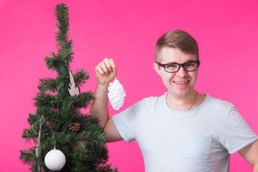 Christmas, holidays and people concept- young happy man show christmas decorations on christmas tree over the pink background.