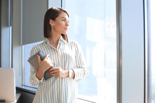 Attractive business woman in smart casual wear looking away and smiling while standing in the office.