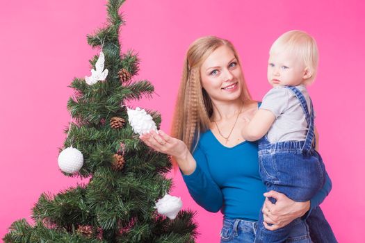 Christmas, holidays and people concept - young happy woman with her daughter on hands show decorations on christmas tree.