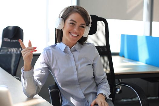 Young woman having a break and listening music in headphones sitting on working place