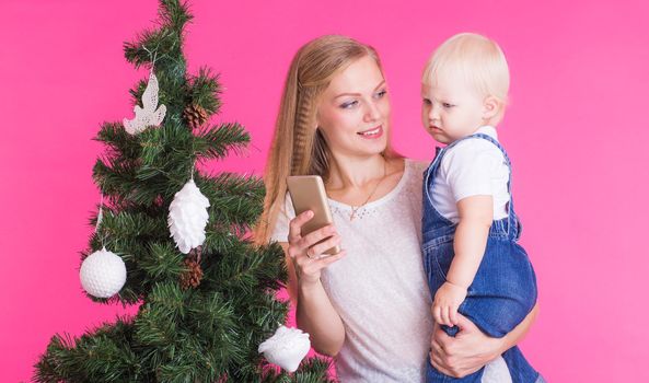 Mother and little daughter taking a selfie near Christmas tree.