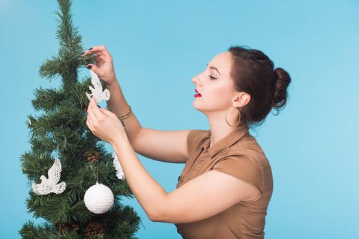 People, holidays and christmas concept - woman decorating christmas tree on blue background.