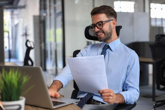 Young man is working with papers while sitting in the office. Successful entrepreneur is studying documents with attentive and concentrated look.