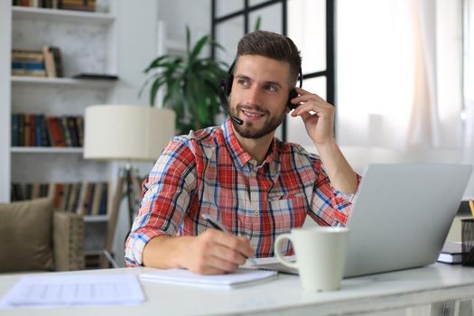 Happy young man in earphones working on laptop from home during self isolation