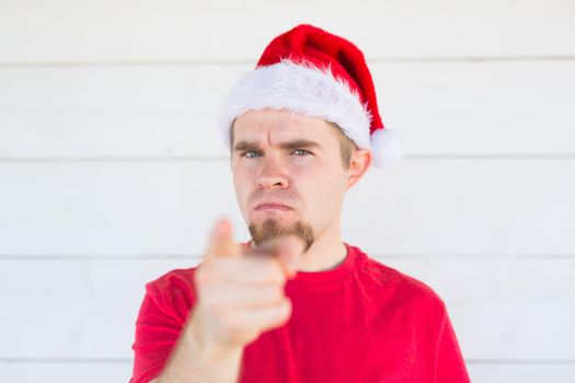 Christmas, people, emotions concept - dissatisfied angry santa in christmas hat pointing at the viewer.