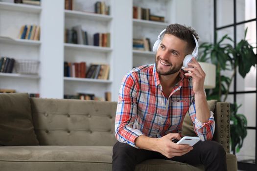 Attractive young man relaxing on a couch at home and using mobile phone for cheking social nets