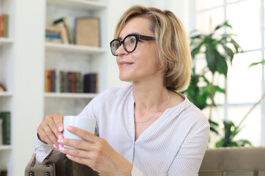 Mature blond woman in couch having a tea or coffee