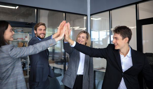 Happy people standing in office and giving high five to their colleagues