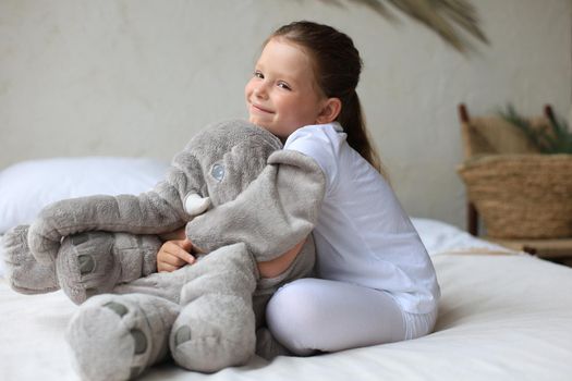 Sweet little girl sitting on her bed at home with toy elephant
