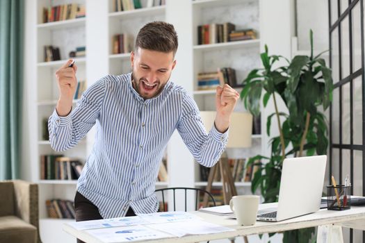 Handsome businessman is keeping arms raised and expressing joyful at office