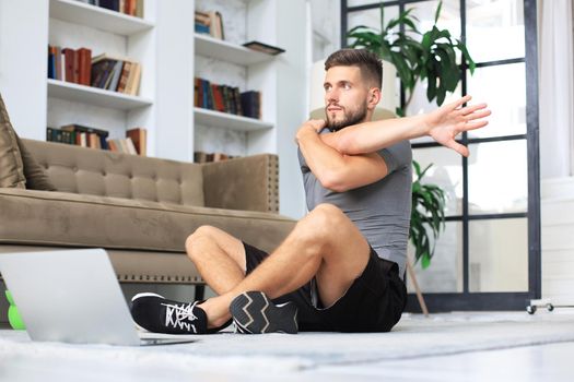 Handsome man doing stretching exercise at home during quarantine. Concept of healthy life