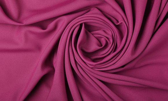 Close up abstract textile background of spiral shaped purple pink folded pleats of fabric, elevated top view, directly above