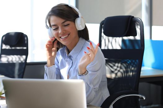 Portrait of beautiful young woman working on computer and chatting sitting in earphones