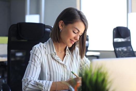 Beautiful business woman is writing something down while sitting in the office desk.