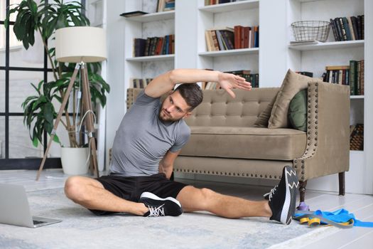 Handsome man doing stretching exercise at home during quarantine. Concept of healthy life