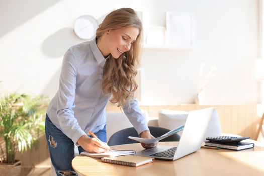 Confident young businesswoman with a friendly smile standing behind her desk in a home office