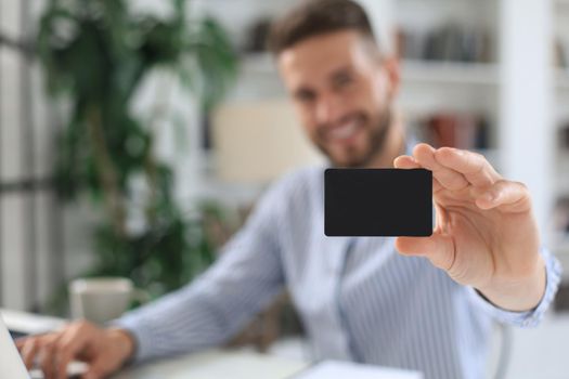 Young man sitting in office and pays by credit card with his tablet