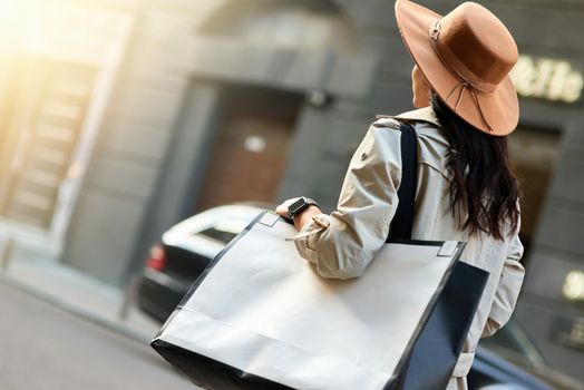 Young woman wearing hat with big shopping bag walking city streets. Fashion, people lifestyle concept