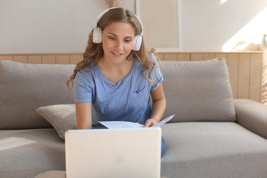 Smiling girl sit near couch watching webinar on laptop. Happy young woman study on online distant course