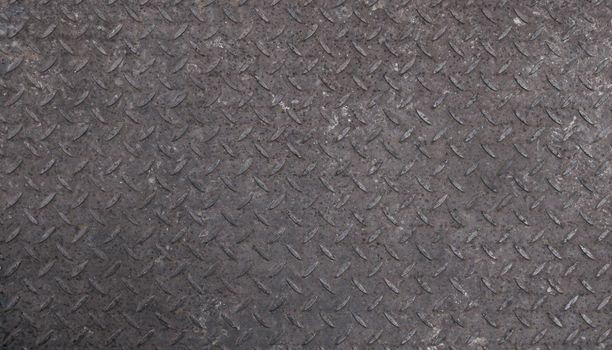 Background texture of gray industrial anti slip embossed metal steel plate surface with diagonal bumps of diamond pattern, close up