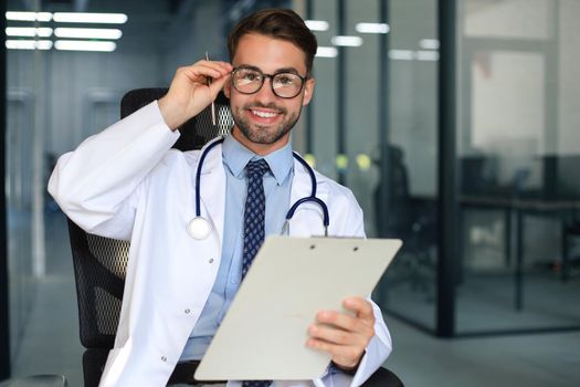 Handsome friendly young doctor on hospital corridor looking at camera, smiling