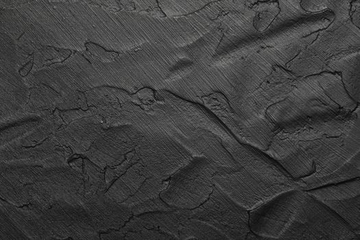 Black abstract background texture of uneven grunge surface with brushstrokes of plaster and paint