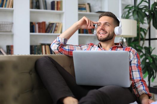 Young tired freelancer in casualwear sitting on sofa in front of laptop