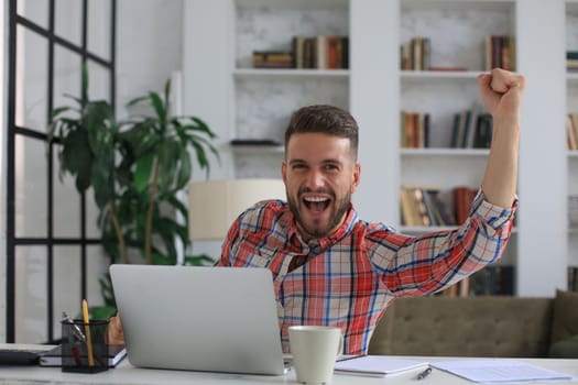 Handsome businessman is keeping arms raised and expressing joyful at home office