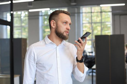 Handsome business man using a voice recognition app in office